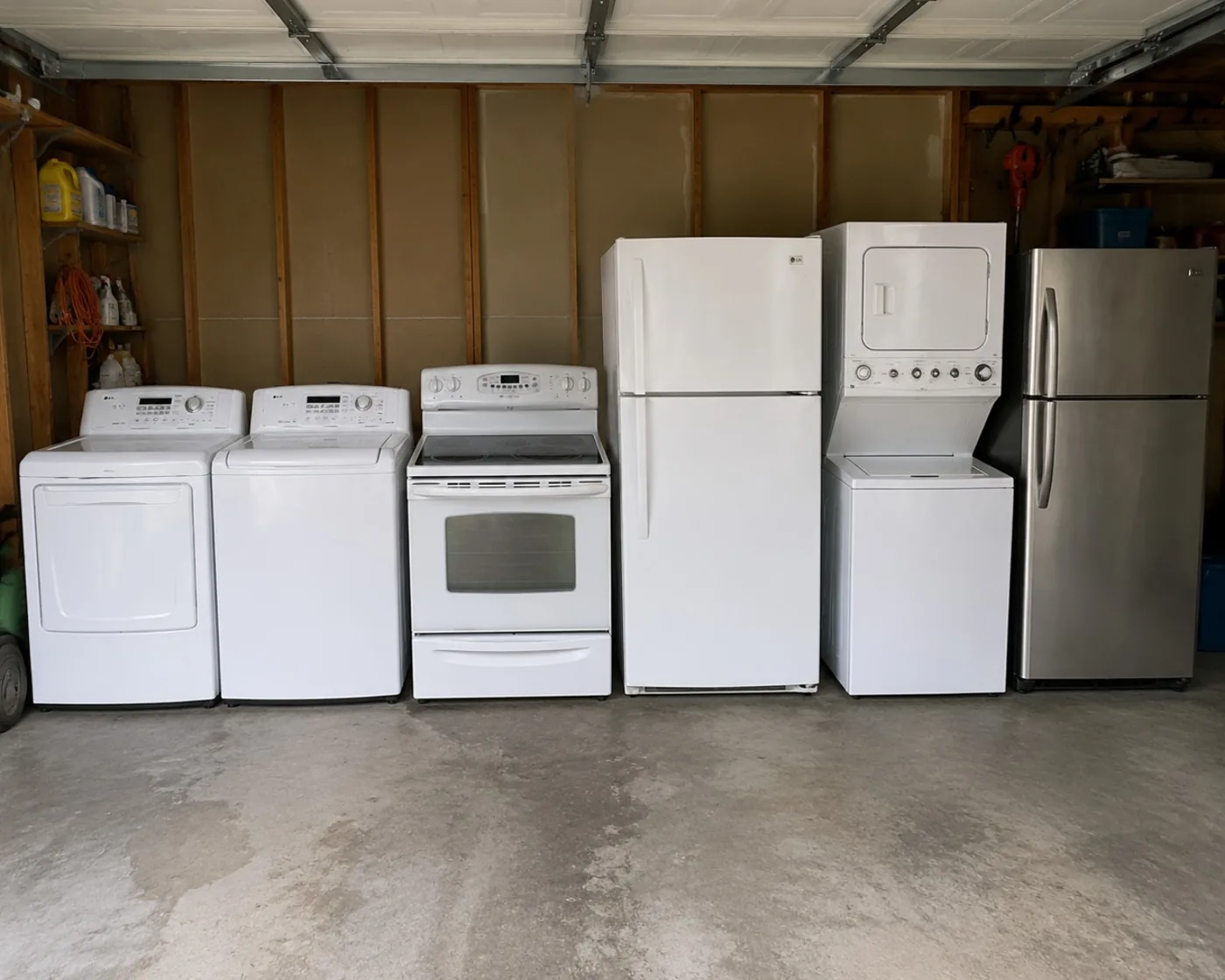 Six major appliances together in a garage: washer, dryer, electric stove, refrigerators and laundry center